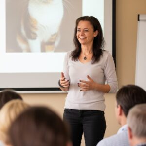 Carmen Schell steht vor einer Schulungsgruppe und erläutert ein Katzenthema
